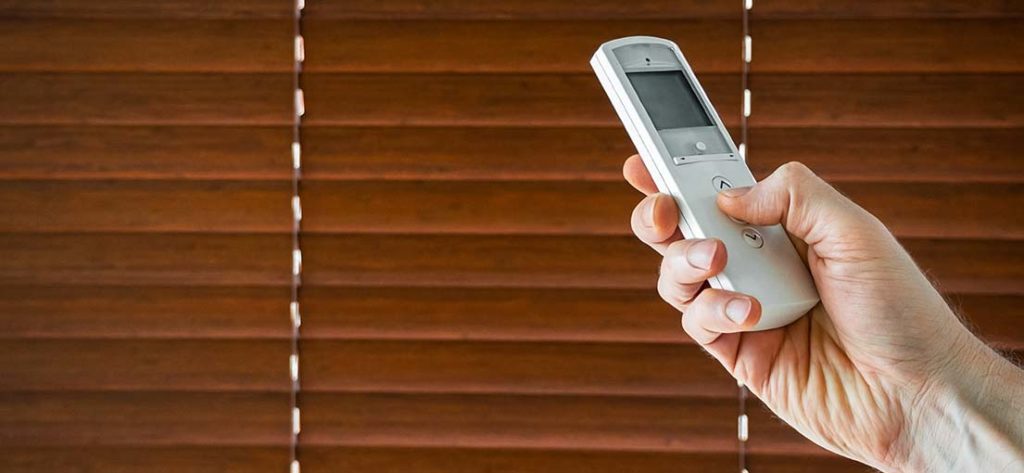 A hand holding remote clicker for motorized blinds