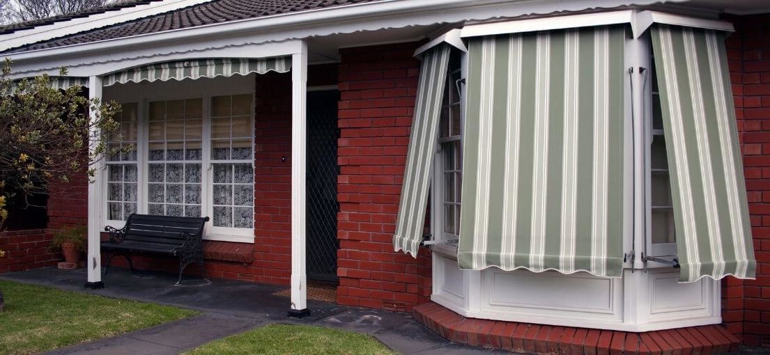 Striped fabric awning extending over a large bay window.