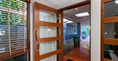 A view through an open wooden door leading into a modern home interior with large glass windows and a glimpse of a dining area