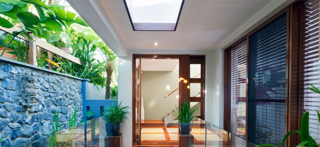 Contemporary home entrance with an open wooden door, highlighting a bright and airy interior with glass windows.