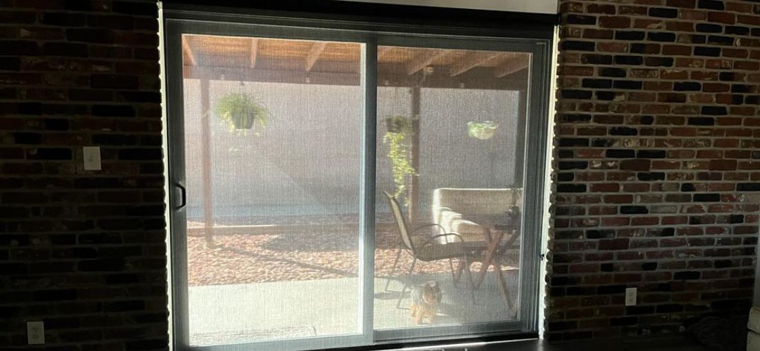 Close-up of black screen roller shades installed on a patio door for privacy and sunlight control.