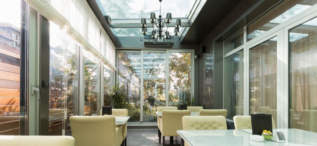 Interior view of restaurant terrace with ceiling-to-floor windows covered by light Roman shades, enhancing the airy ambiance.