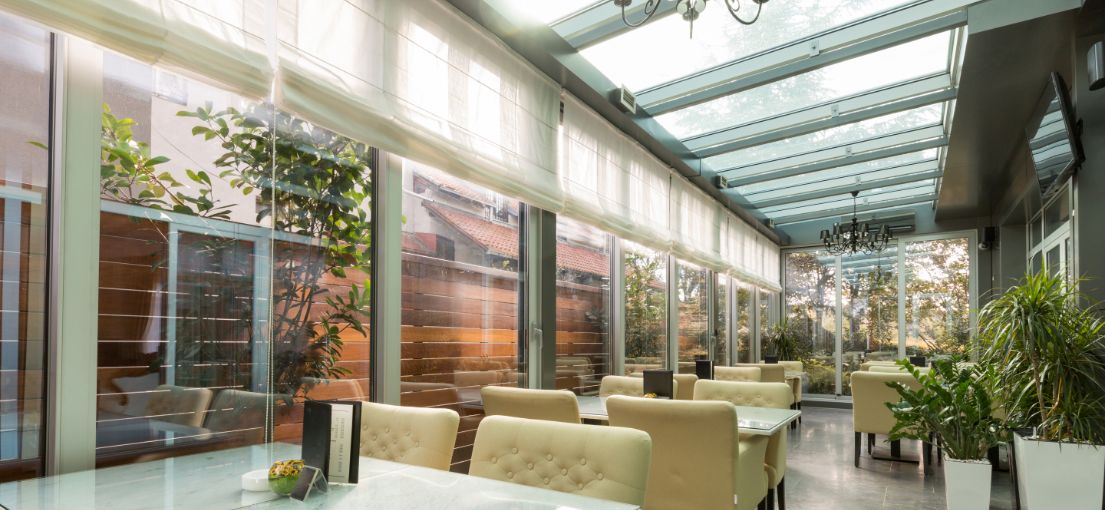 Spacious restaurant terrace with custom light Roman shades installed on tall windows, creating a serene and stylish atmosphere.