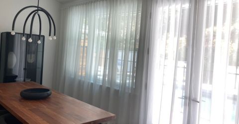 Dining room with custom sheer curtains along wide windows, allowing natural light to softly filter in.