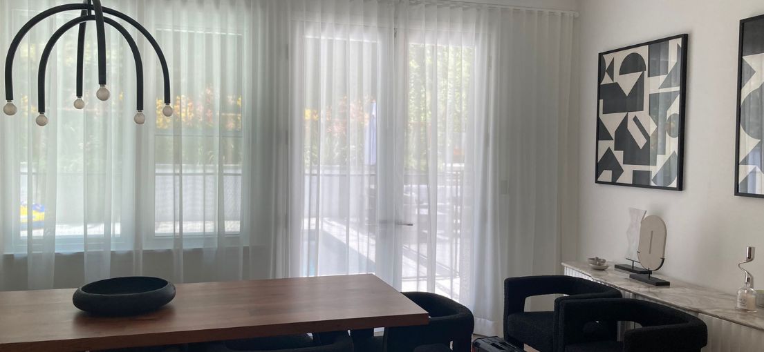 Elegant dining room with custom sheer curtains installed on wide windows, providing a soft and light-filled ambiance.