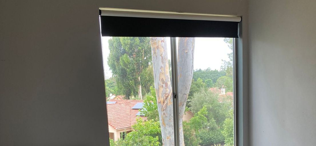 Master bedroom with black blackout shades fully rolled up on the window.