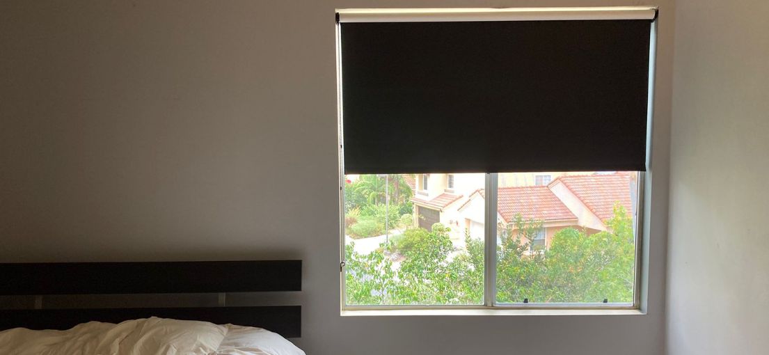 Guest bedroom featuring black blackout shades half down on the window.