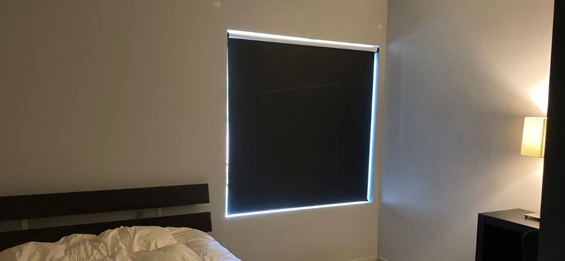 Modern bedroom with black blackout shades fully rolled down on the window.